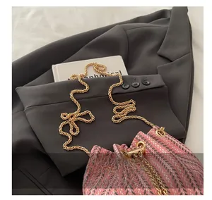 Close-up of pink tweed bucket bag featuring gold chain strap on grey blazer background