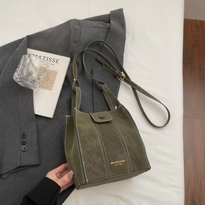 Retro dark green matte bucket bag with adjustable strap on a grey suit jacket