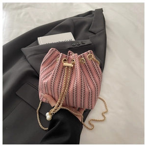 Detailed macro view of pink tweed bucket bag with golden chain and pearl drawstrings