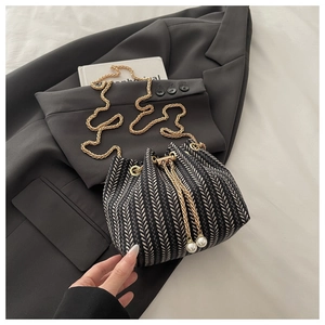 Detail of woven bucket bag featuring gold chain strap and elegant pearl drawstring accents