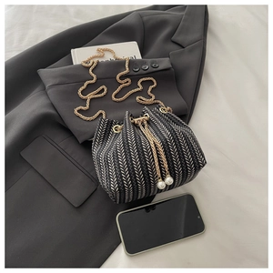Detail of herringbone woven bucket bag with gold chain and elegant pearl drawstring accents
