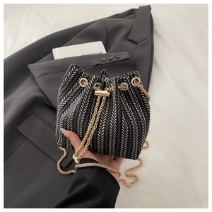 Macro view of woven herringbone bucket bag featuring gold chain and pearl embellishments