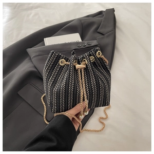 Detailed view of black and white woven bucket bag with pearl drawstring and gold chain