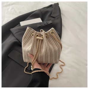 Detail of woven bucket bag featuring drawstring closure, gold chain and pearl charm