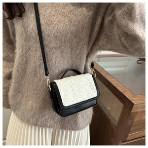 Detail of a contrast faux shearling saddle bag worn with a casual brown knit sweater