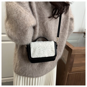 Detail shot of a black leather saddle bag with white faux fur trim and gold hardware strap