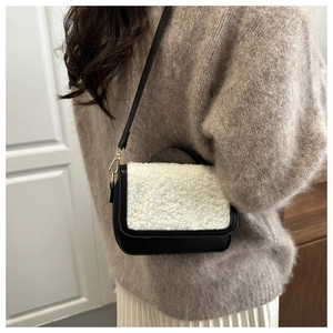 Detail of a chic black leather and white faux fur crossbody bag with golden hardware