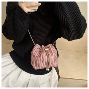 Detail of striped knit bucket bag with golden chain strap and pearl drawstring charms