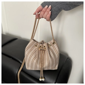 Detail of woven bucket bag featuring gold chain drawstring and elegant pearl charms