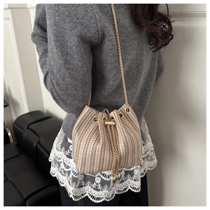 Detailed view of woven straw bucket bag with gold chain and white lace trim detail