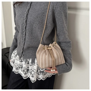 Detail of woven bucket bag with V-shaped texture, gold chain and pearl drawstring