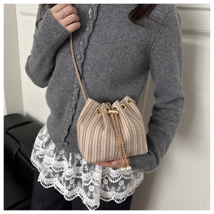 Detail of beige straw bucket bag with V-shaped weave, gold chain, and pearl drawstring charms
