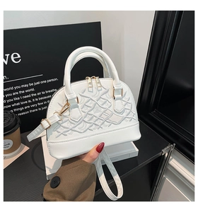 Detail of white shell handbag with intricate vine embroidery and golden zipper hardware