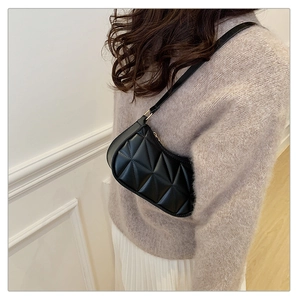 Close-up of black quilted shoulder bag with diamond stitching on a female model
