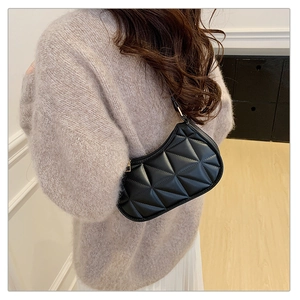 Quilted black leather crescent underarm bag worn by model with minimalist beige outfit