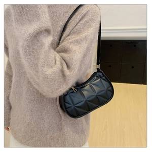 Detail of black glossy shoulder bag with rhombus embossed pattern on a soft sweater