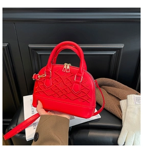 Detail of red shell-shaped handbag with intricate embroidery and gold dual zippers