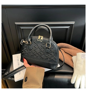 Close-up of black shell bag with embroidered texture and gold zipper details