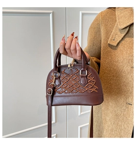 Detail of coffee shell bag with vine embroidery held by model in wool coat
