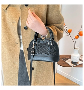 Detailed close-up of a black embossed shell bag with golden zipper and leather handle
