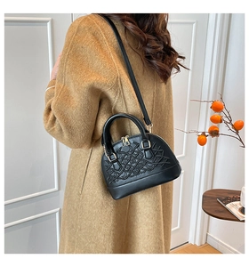 Black Boston bag with geometric stitching shown on a model wearing a camel wool coat