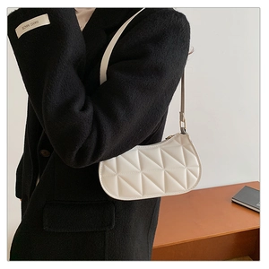 Close-up of minimalist white quilted crescent bag styled on a black coat shoulder