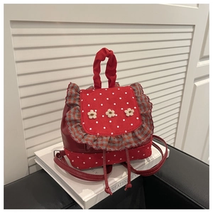 Detail of red polka dot backpack with 3D floral accents and ruffle edges on a white sofa