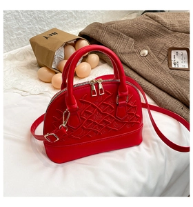 Top view of a red quilted shell handbag with gold zippers on white fabric background