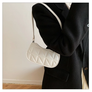 Close-up of white geometric quilted shoulder bag worn with a black wool coat