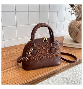 Detail of dark brown shell handbag featuring geometric embroidery and metal zipper on wood