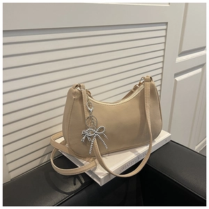 Detail of matte beige underarm bag featuring a metallic silver bow chain on white book
