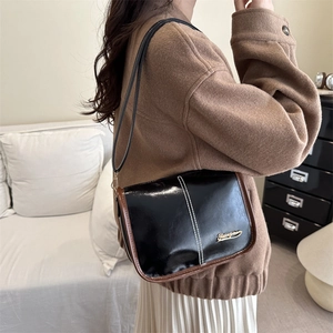 Sac à bandoulière en cuir noir brillant avec bordure marron et logo doré sur mannequin