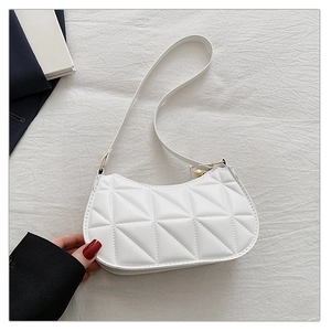 Top view of white quilted crescent shoulder bag with gold hardware on linen fabric