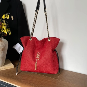 Sparkly red glitter tote bag with golden logo and chain strap on a wooden desk