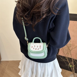 Mint green and white cherry crossbody bag worn by a model in a navy sweatshirt