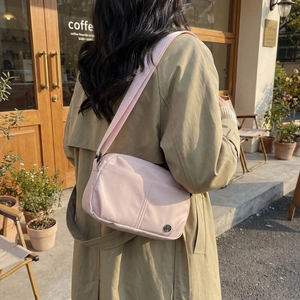 Pink nylon crossbody bag with round metal logo shown in casual outdoor setting