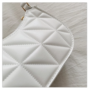 Detail of white quilted handbag featuring geometric triangle stitching and gold metal hardware