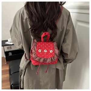 Close-up of red polka dot backpack with ruffled trim and white floral accents on the flap