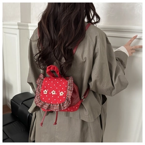 Detail of red polka dot mini backpack with floral accents and ruffle trim on model