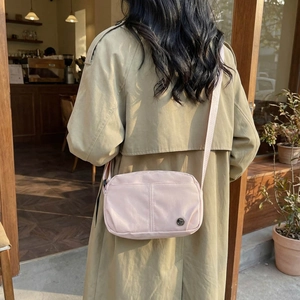 Minimalist light pink crossbody bag with adjustable strap worn by a woman in a trench coat