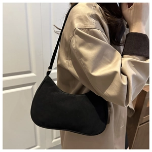 Detail of minimalist black matte suede hobo bag worn with a casual autumn trench coat