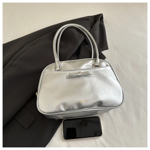 Close-up of silver glossy handbag featuring a bow detail and fashion text on fabric background