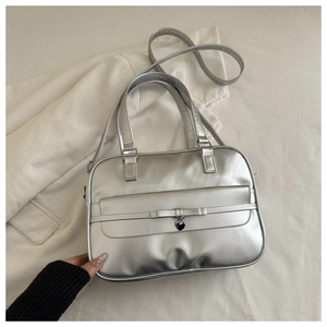 Detail of silver matte underarm bag featuring a bow accent and a heart-shaped metal pendant