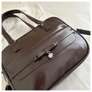 Close-up of brown faux leather bag featuring a silver heart charm and polished texture