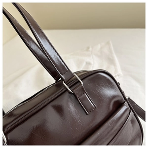 Close-up of dark brown glossy leather bag with reinforced stitching and silver hardware