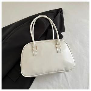 Detailed close-up of white minimalist Boston bag with gold rings on a black blazer