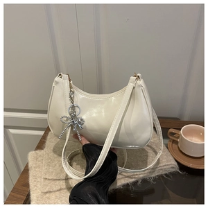 Detailed view of white half-moon bag featuring a silver bow charm and thin shoulder strap