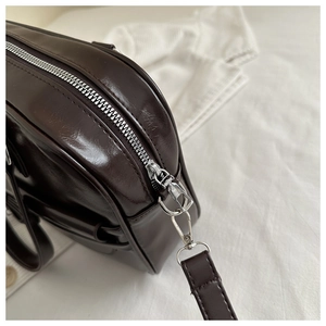 Detail view of silver metal zipper and hook on dark chocolate glossy PU leather bag