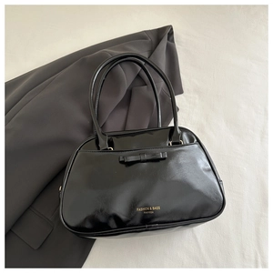 Close-up of black glossy pillow bag with bow detail on a grey suit jacket backdrop