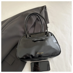 Detail of black glossy PU shoulder bag with bow decoration and slim handles on gray suit